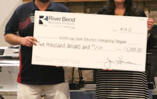 River Bend Business Products employee holding up a donation of $2,000 to the United Way with a representative from the United Way